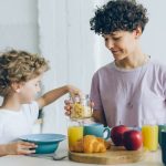 A mother and her son sharing a healthy breakfast at home, featuring cereal, juice, and milk.